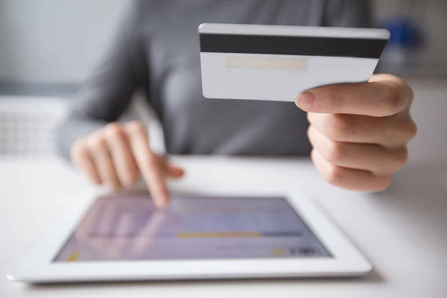 Eine Person hält eine Kreditkarte vor einem Tablet.